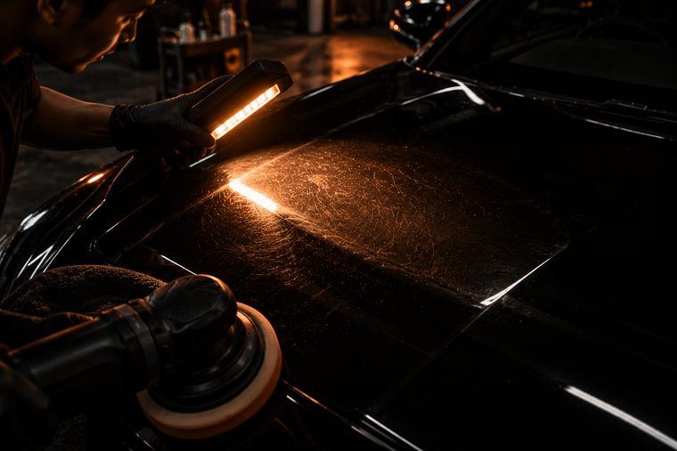 An inspection light raking across a black bonnet, revealing a web of fine swirl marks in one bright ellipse.
